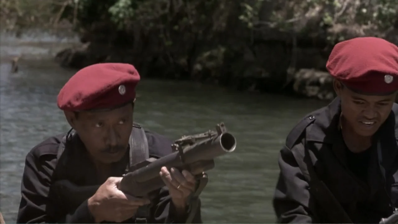 Behind Enemy Lines (2001) movie still: medium — Two men in tactical gear patrol a river in a small boat. One man holds a large grenade launcher…
