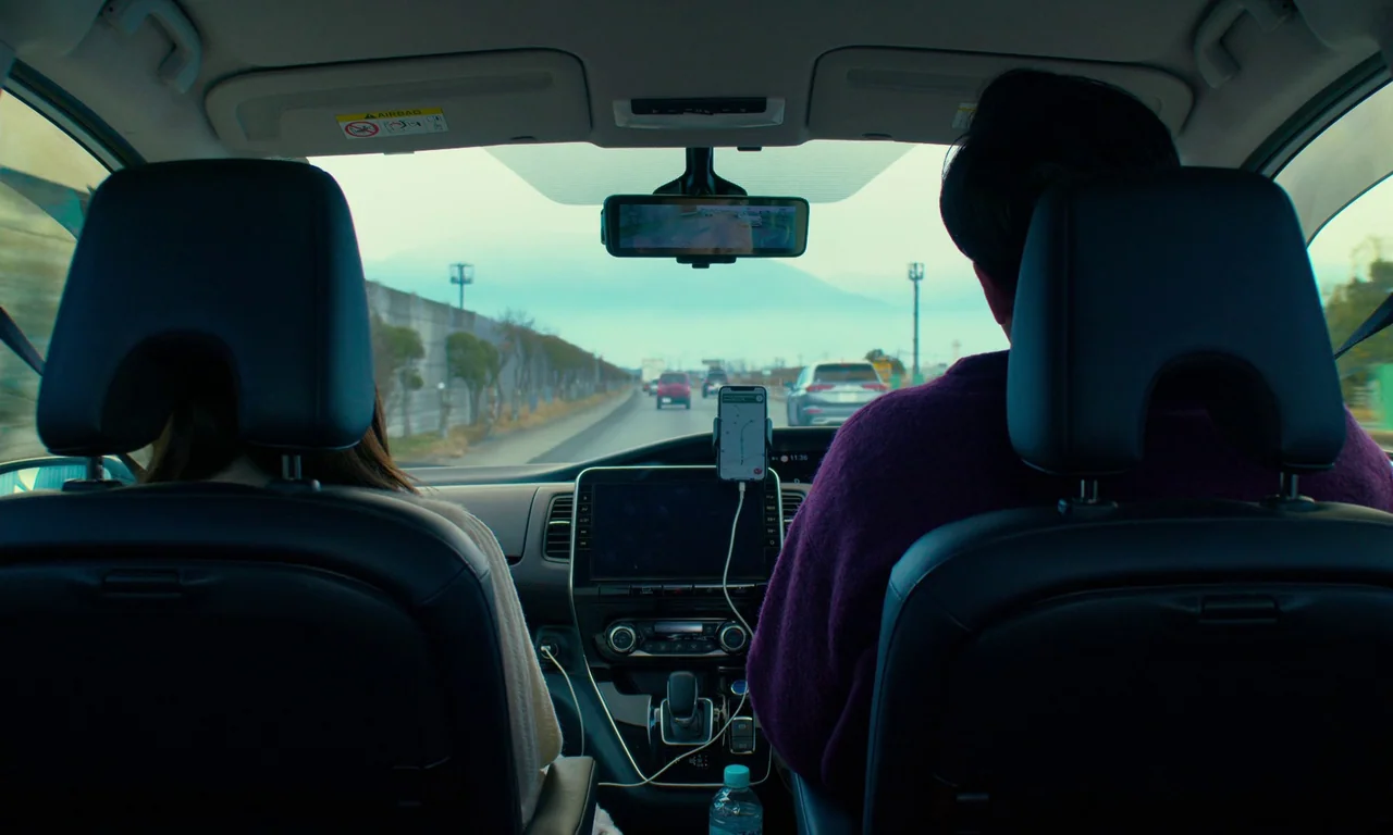 Evil Does Not Exist (2023) movie still: medium — The interior of a modern vehicle showing two people seated in the front seats. Outside the…