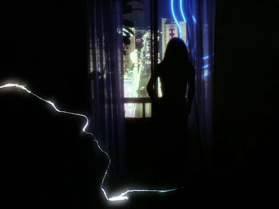 One From The Heart (1982) movie still: wide — A dark hotel room interior at night overlooks a brightly lit city street. A silhouette of a woman…