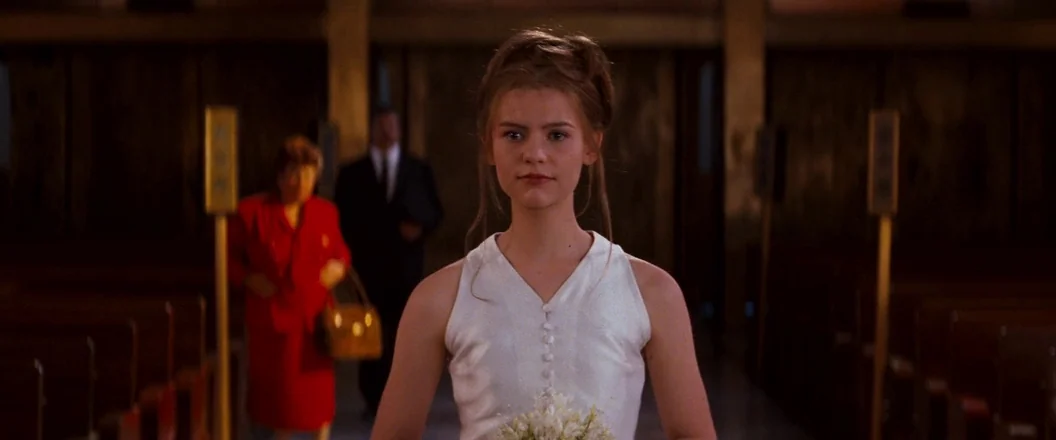 Romeo + Juliet (1996) movie still: medium — A spacious church interior features rows of dark wooden pews under high ceilings. A young woman stands…