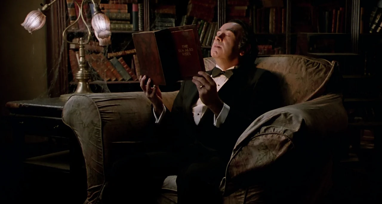 The Addams Family (1991) movie still: medium — A dark, dimly lit home library is lined with rows of aged, leather-bound books. A middle-aged man in…