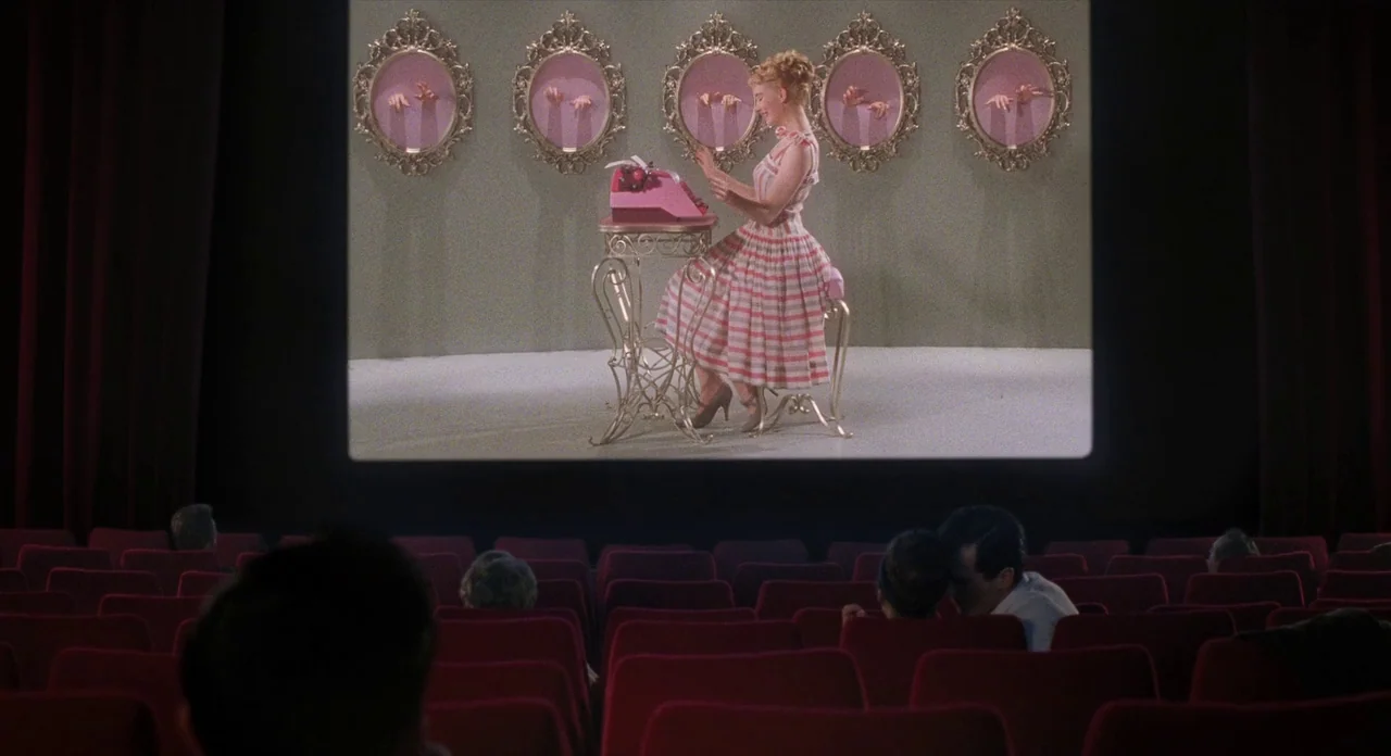Populaire (2012) movie still: wide — A view from within a dark movie theater looking at a screen playing a film. The film shows a woman in a striped…
