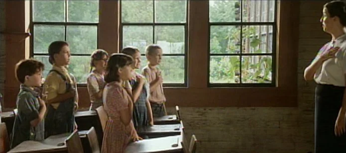 The Neon Bible (1995) movie still: medium — A rural schoolhouse interior features wooden desks and large windows overlooking trees. Five children…