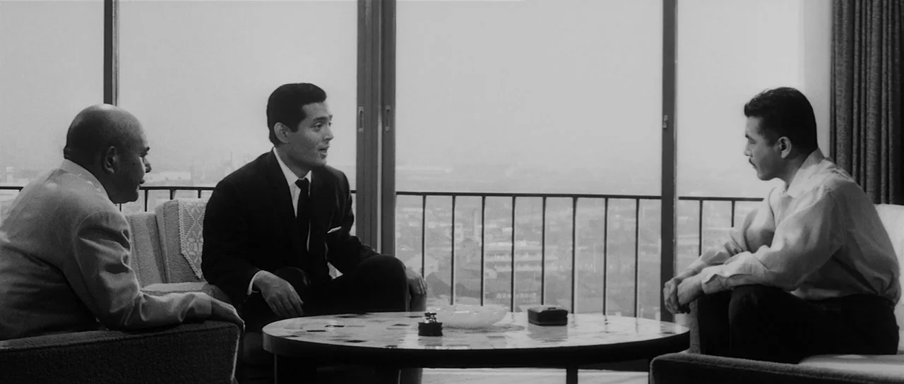 High and Low (1963) movie still: medium — A high-rise room with floor-to-ceiling windows overlooks a city landscape. Three men sit on chairs around…