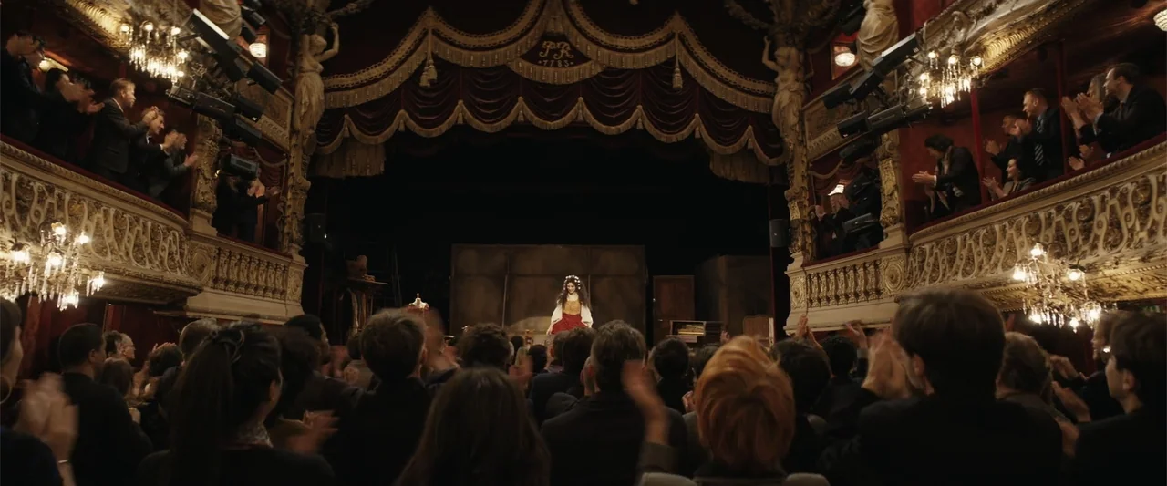 Dogman (2023) movie still: wide — A historic opera house interior features tiered balconies with ornate gold leaf carvings. A performer stands in…