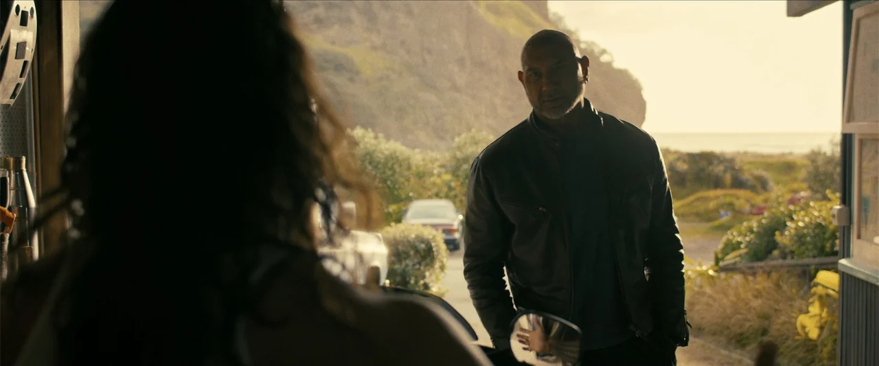 The Wrecking Crew (2026) movie still: medium — A man stands in the doorway of a coastal building during sunset. He looks at a person whose back is…
