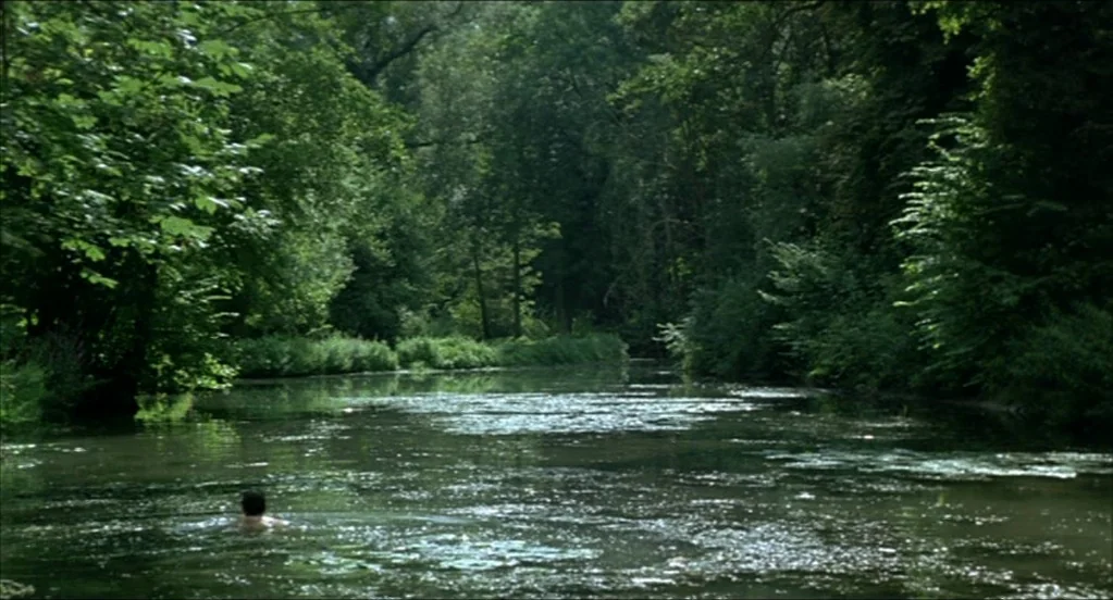 On War (2008) movie still: wide — A slow-moving river flows through a dense, lush green forest with thick canopy cover. A lone individual swims in…