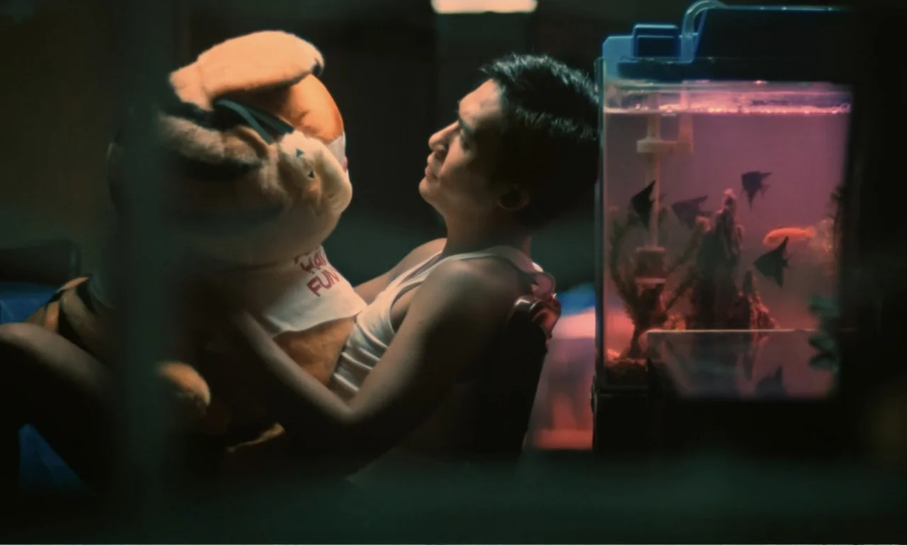 Chungking Express (1994) movie still: medium — A dark, cluttered room contains a fish tank casting a soft purple light. A young man in a white tank…
