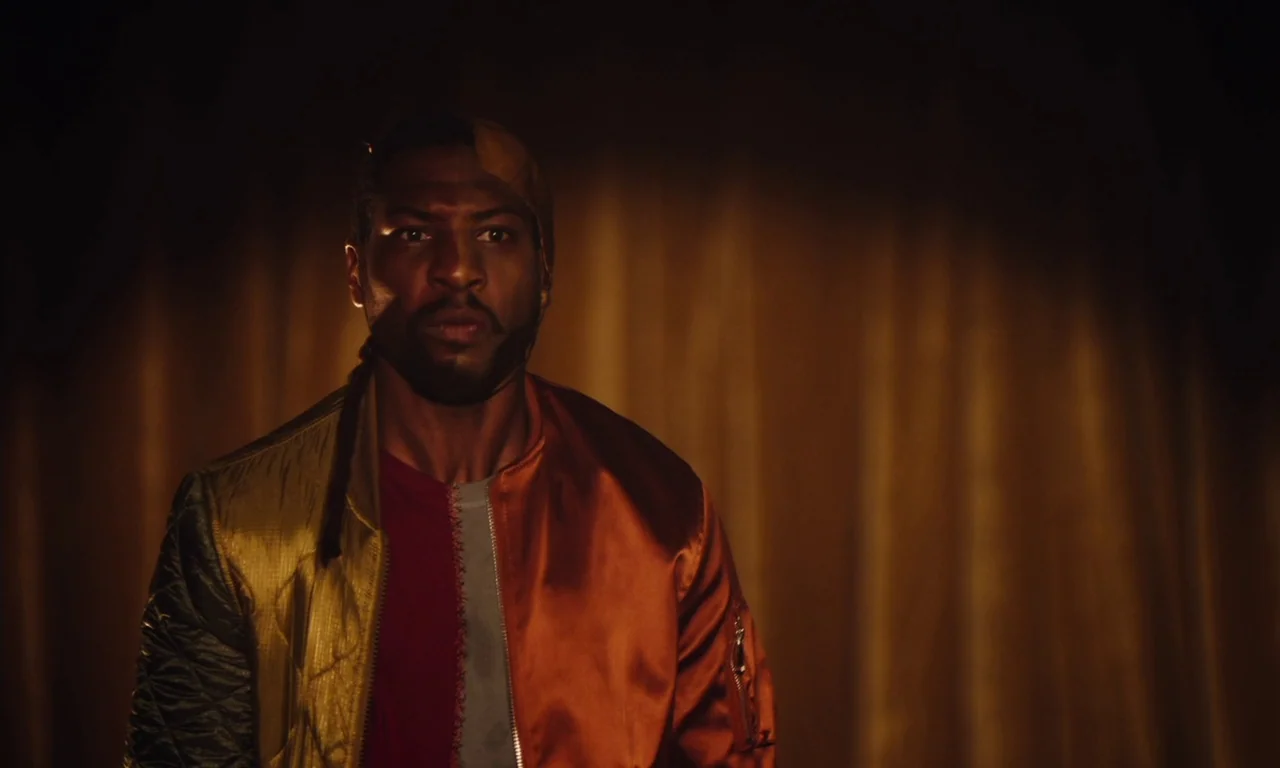 The Last Black Man in San Francisco (2019) movie still: medium — A man stands in front of dark, draped fabric curtains in a dimly lit space. The…