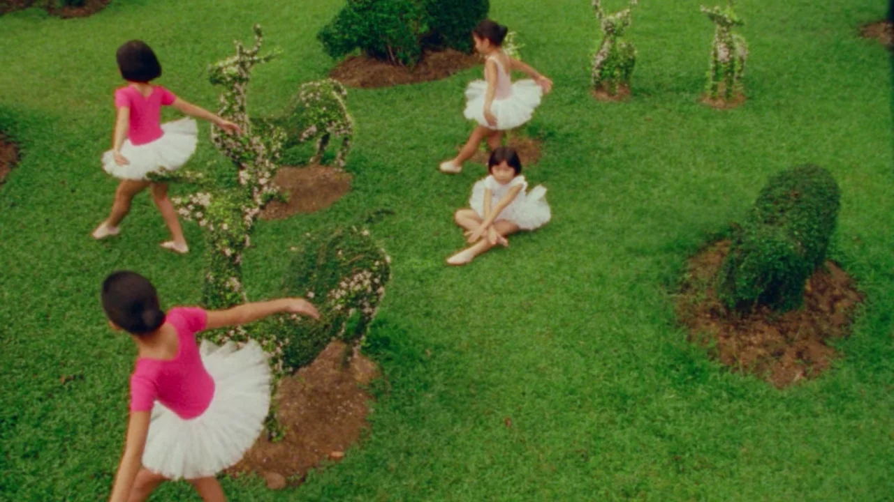 Shirkers (2018) movie still: wide — A manicured lawn features several sculpted green animal topiaries and well-kept grass. Four young girls dressed…