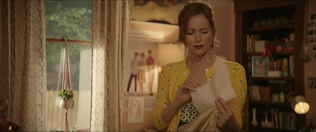 Blockers (2018) movie still: medium — A cozy bedroom contains a window with curtains, a bookshelf, and framed wall art. A woman in a yellow sweater…