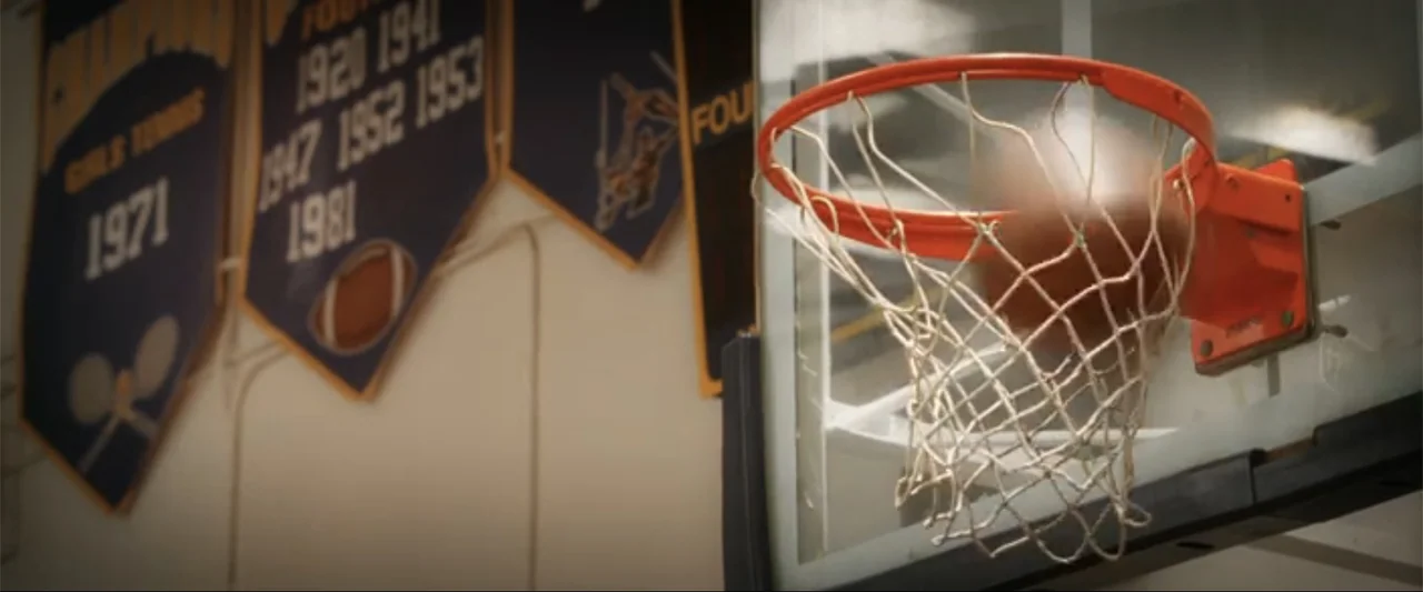 17 Again (2009) movie still: closeup — A gymnasium wall features athletic championship banners hanging near a glass basketball backboard. A…
