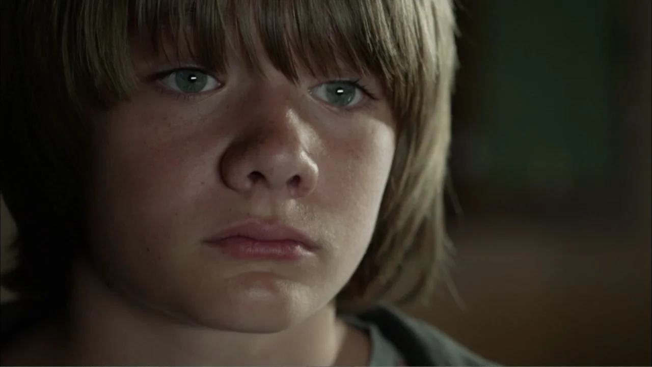 Dark Skies (2013) movie still: closeup — A close-up view shows a young boy's face in an undefined interior space. The subject stares directly ahead…