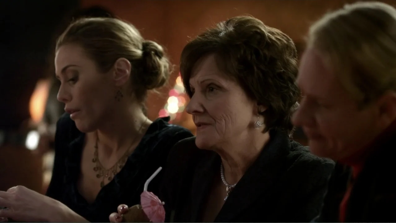 It's Christmas, Carol! (2012) movie still: medium — A dimly lit indoor space features three women gathered around a table. The group holds a…