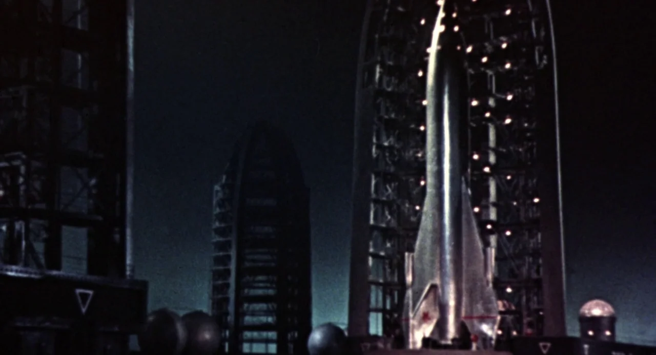 Queen of Blood (1966) movie still: establishing — A nighttime launch pad features metallic rockets contained within tall, illuminated scaffold…