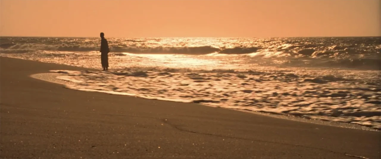Charlie's Angels (2000) movie still: wide — A wide shot shows a sandy beach with breaking ocean waves under a warm sky. A single man stands near the…