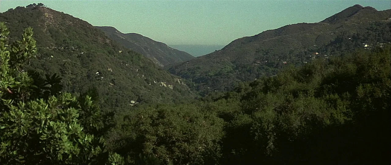 Scream 3 (2000) movie still: establishing — A wide canyon landscape filled with dense green shrubbery and sloping hillsides under daylight.…