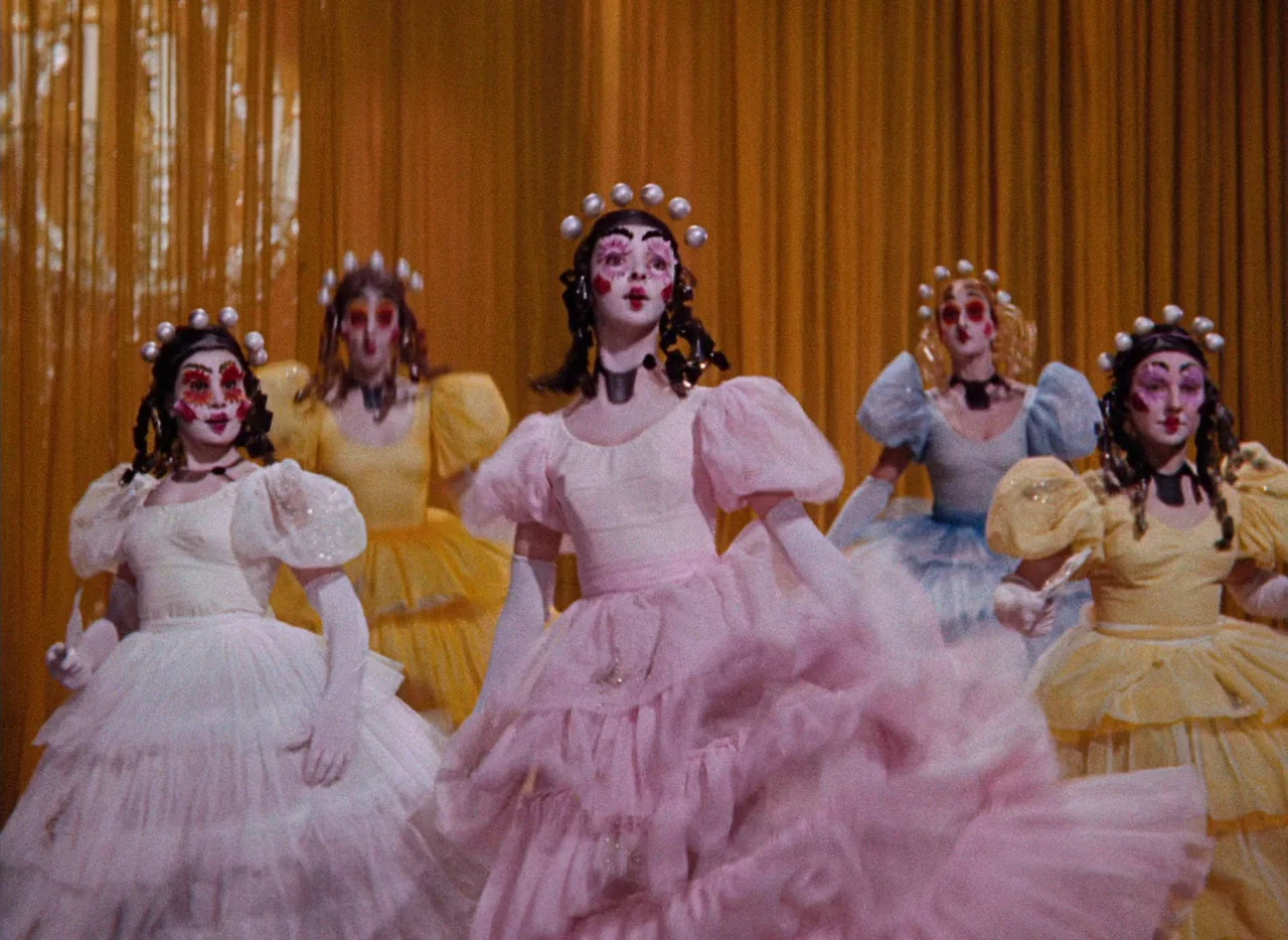 The Tales of Hoffmann (1951) movie still: fullbody — A group of dancers performs on a stage framed by golden pleated curtains. Five women in…