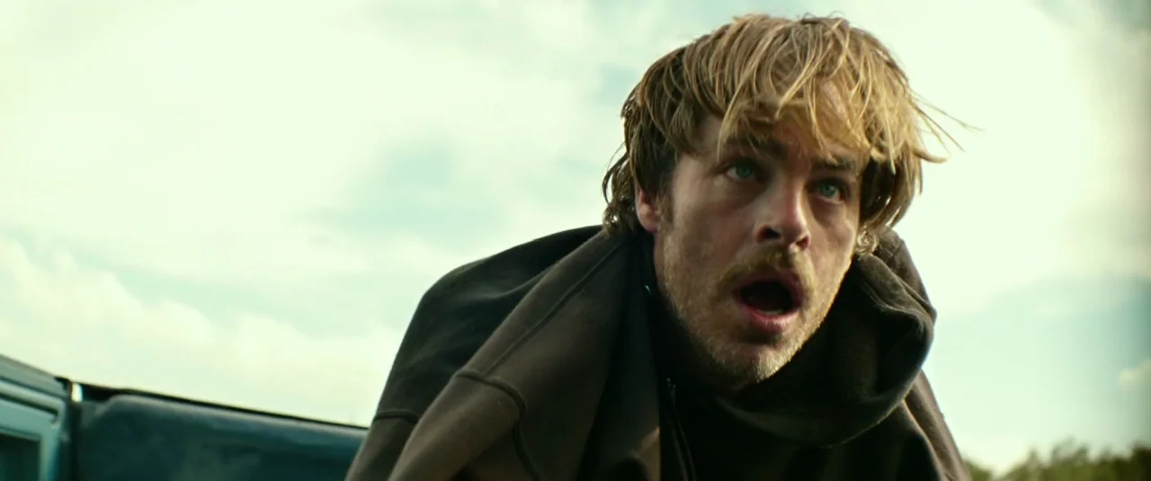 Hell or High Water (2016) movie still: medium — A man stands in the open bed of a pickup truck outdoors. He looks toward the side with a shocked…