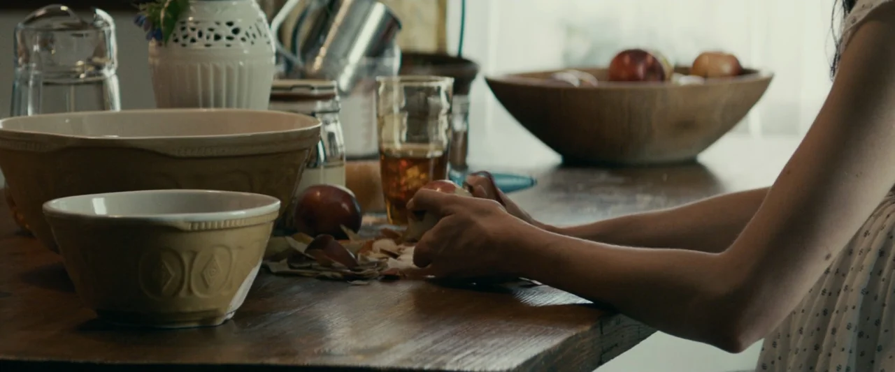 Strange but True (2019) movie still: medium — A rustic wooden table is covered with a ceramic bowl, glass, and apple skins. A person sits at the…