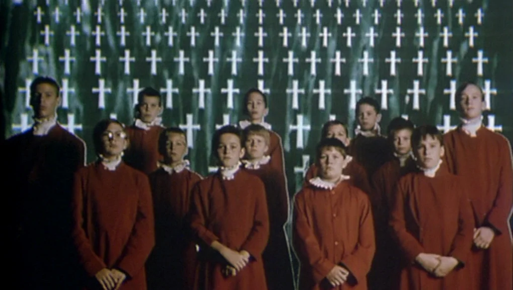 War Requiem (1989) movie still: fullbody — A group of boys dressed in identical red robes stand in a dark space. A large projection of many white…