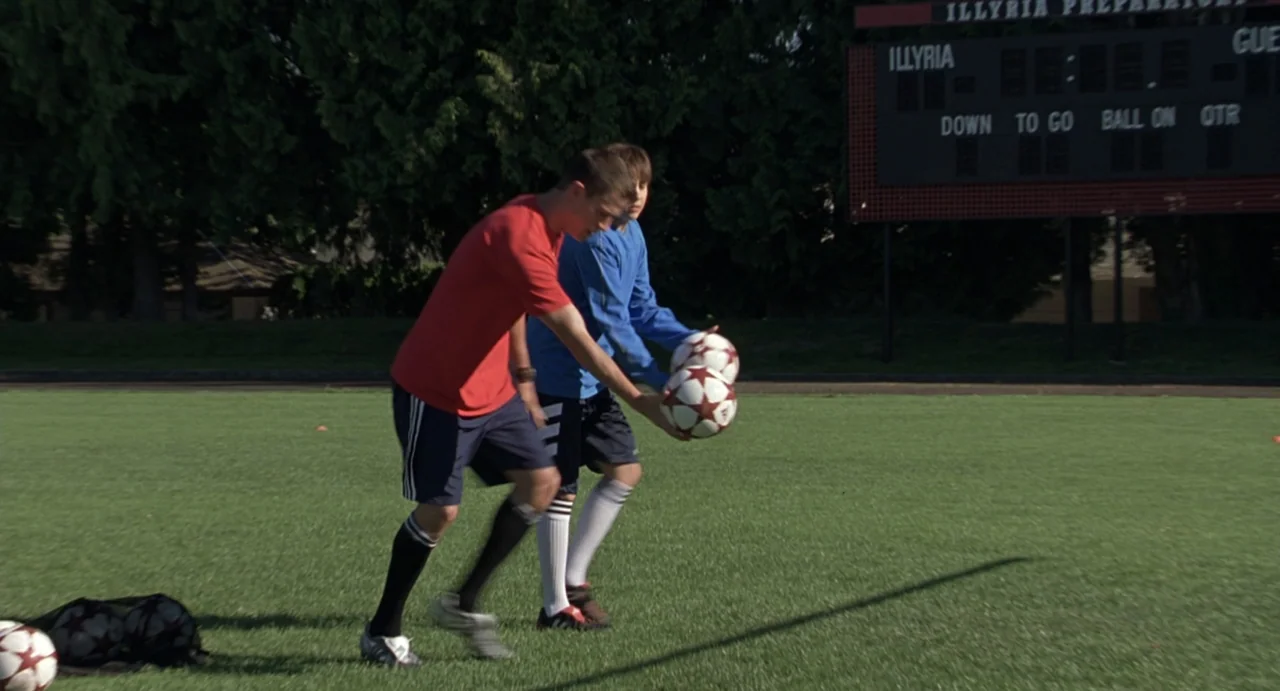 She's the Man (2006) movie still: fullbody — A green sports field features a scoreboard in the background under clear daylight. Two male teenagers…