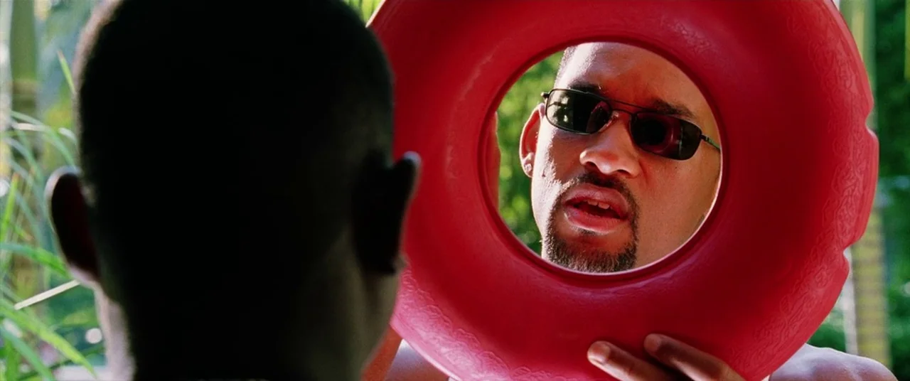 Bad Boys II (2003) movie still: medium — A man looks through the circular hole of a red toy plastic disk. The person viewing is partially obscured…