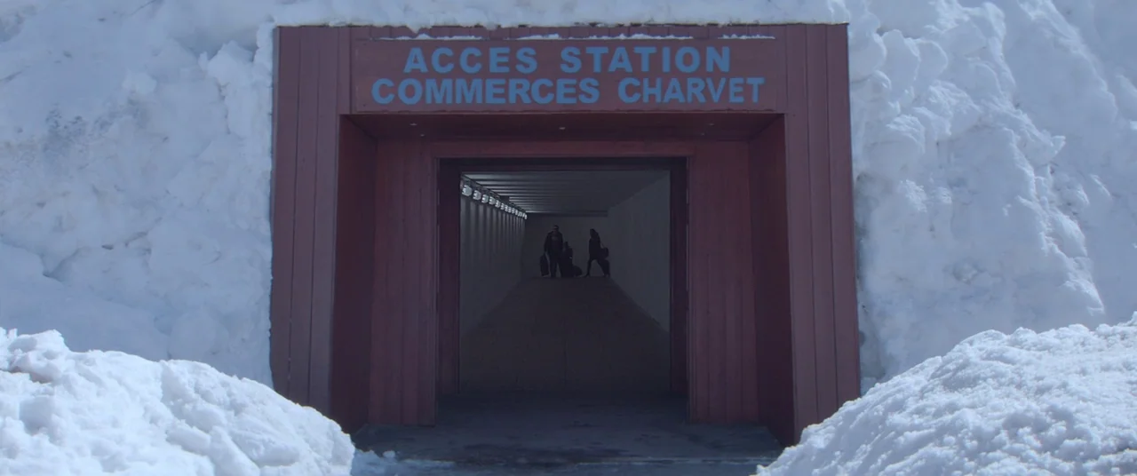 Force Majeure (2014) movie still: wide — A brown tunnel entrance is flanked by high walls of accumulated white snow. A small group of people with…