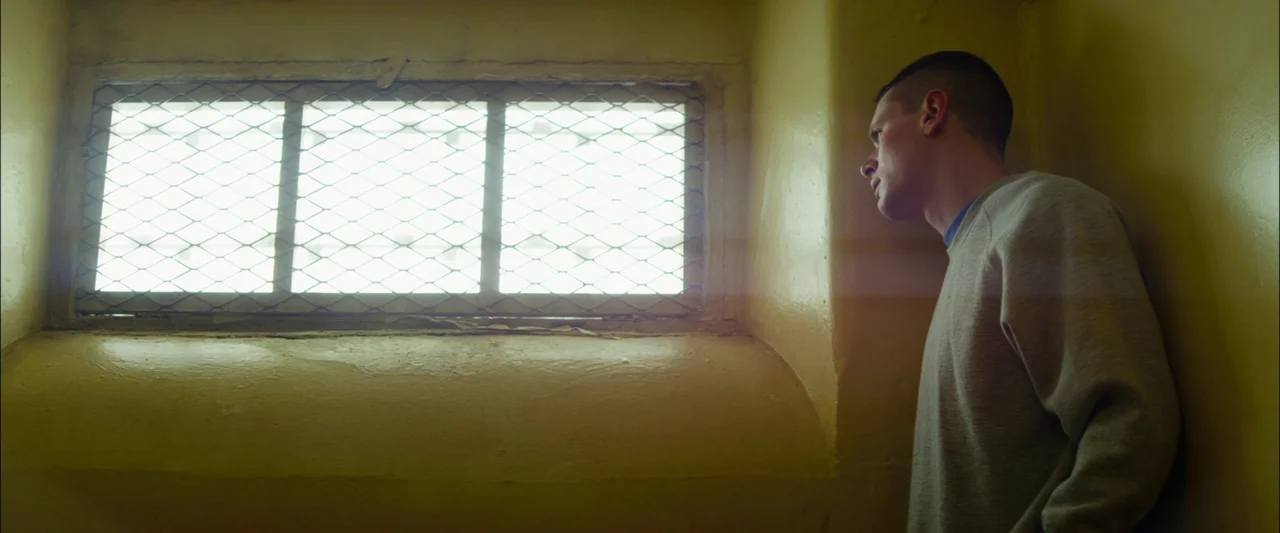 Starred Up (2013) movie still: medium — An interior space with yellow-painted walls features a rectangular window protected by wire mesh. A young…