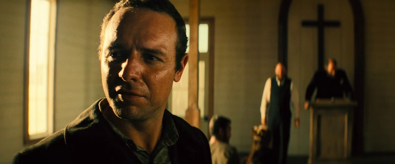 The Magnificent Seven (2016) (2016) movie still: closeup — A rustic church interior features wooden walls and a large cross on the altar. Several…