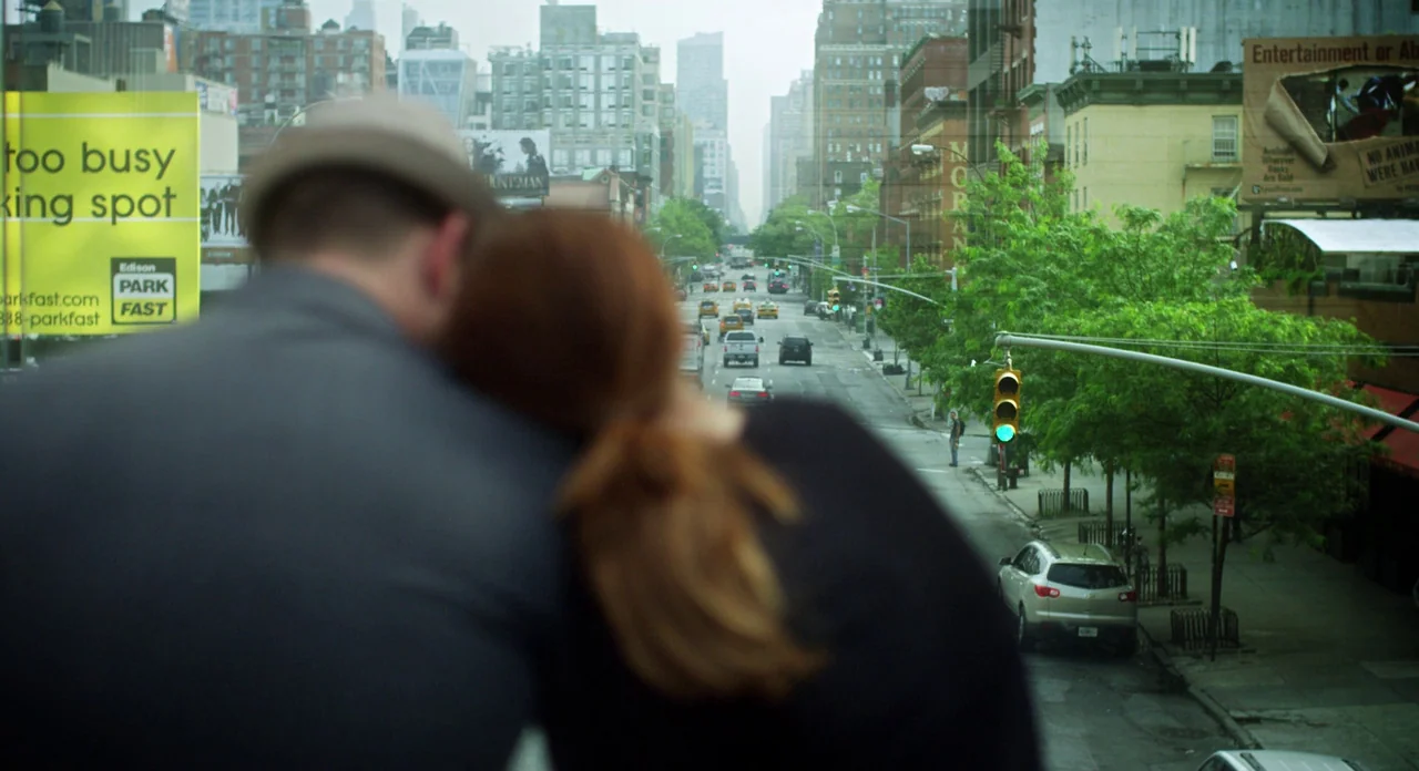 Side Effects (2013) movie still: medium — A bustling New York city avenue viewed from an elevated vantage point with traffic. Two people lean on…