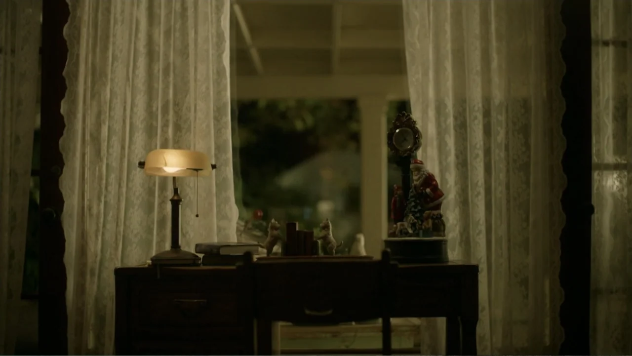 A Carpenter Christmas Romance (2024) movie still: medium — A dark room features a wooden desk placed directly in front of window curtains. A desk…