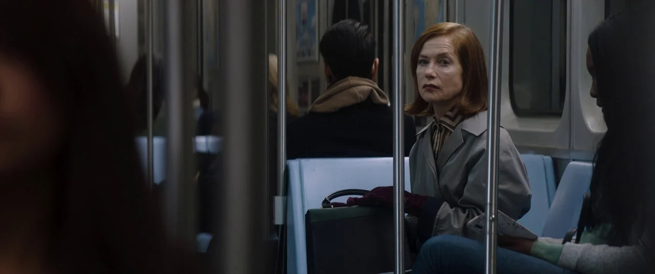 Greta movie still: medium — A quiet commuter subway car with blue plastic seats and vertical stainless steel poles. An older woman with auburn hair…
