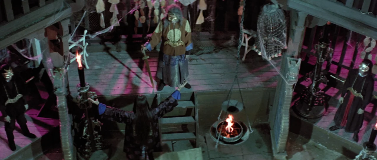 The Legend of the 7 Golden Vampires (1974) movie still: wide — A wooden interior platform covered in cobwebs features two fire pits and masked…