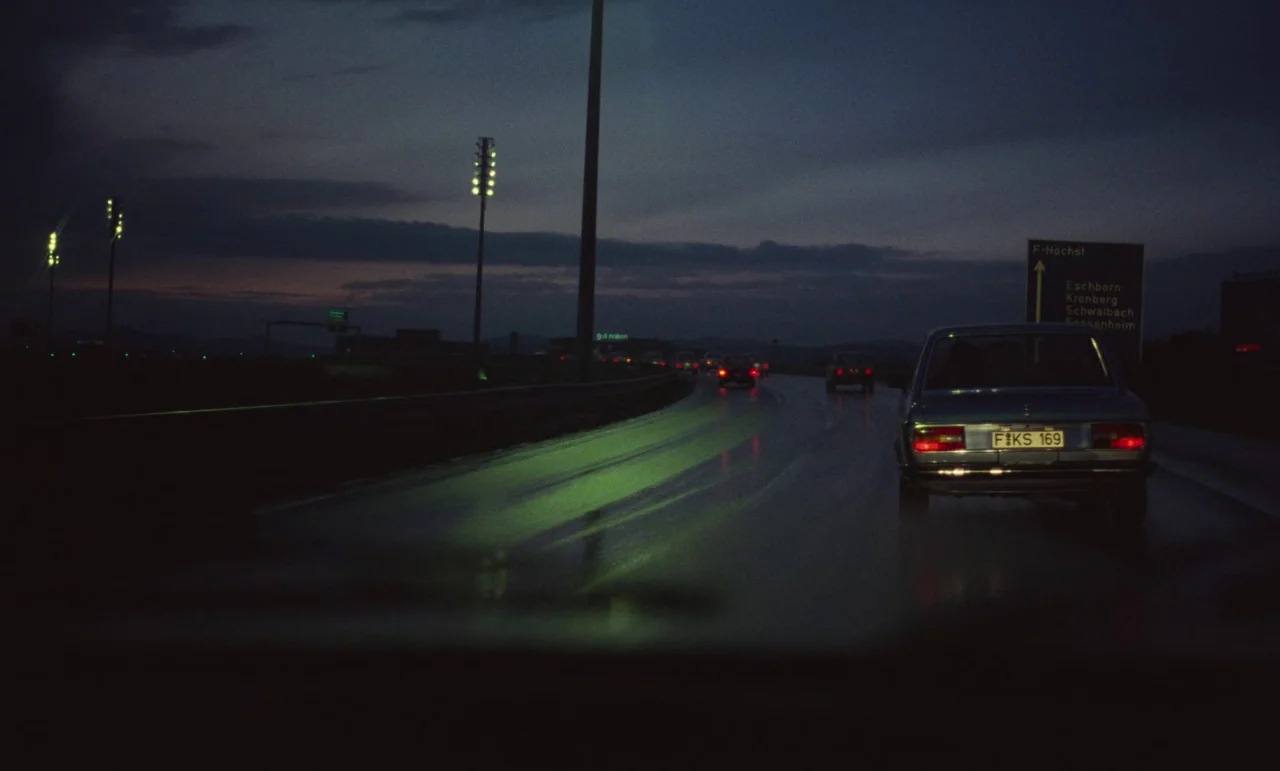 Wrong Move (1975) movie still: wide — A dark, wet asphalt highway at night is illuminated by distant overhead yellow streetlamps. A vintage blue…