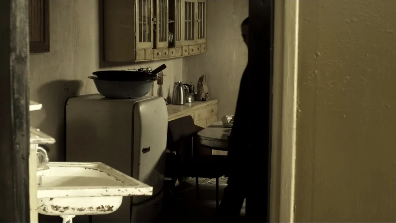 Assassination Games (2011) movie still: medium — A dated 1940s style apartment features a white porcelain sink and a metal vintage refrigerator. A…
