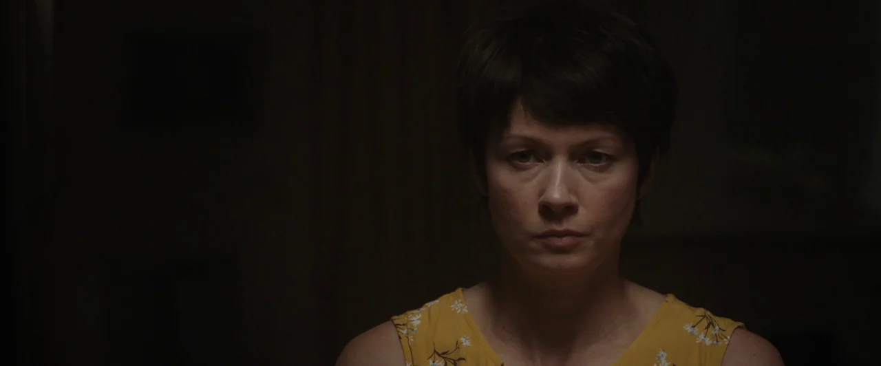 You Are Not My Mother (2021) movie still: closeup — A woman stands in a dark, shadow-filled room with minimal visible detail. She faces the camera…