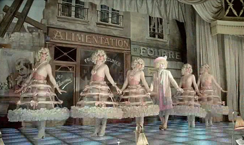 Mr. Klein (1976) movie still: fullbody — A theatrical stage set features painted backdrops of 19th-century French storefronts behind dancers. Five…