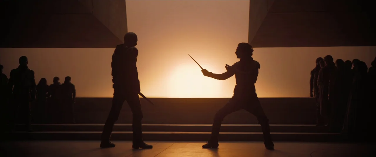 Dune: Part 2 (2024) movie still: wide — A stark, minimalist concrete arena opens out toward a bright, hazy orange sun. Two silhouetted figures face…