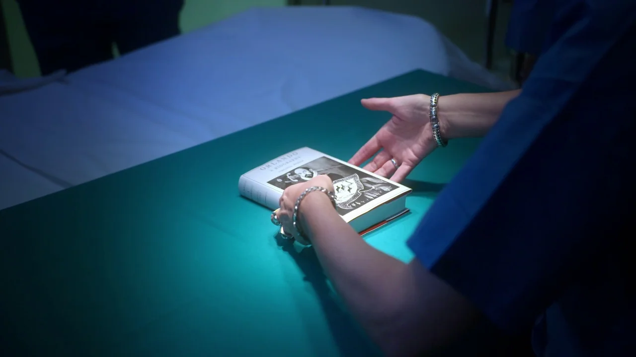 Orlando: My Political Biography (2023) movie still: closeup — A book rests on a bright green surgical drape inside a medical setting. A person in…