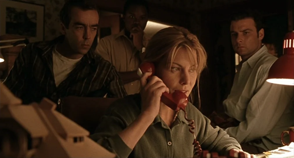 The Hurricane (1999) movie still: medium — A dim room contains four people crowded around a desk with paper documents. A woman uses a bright red…