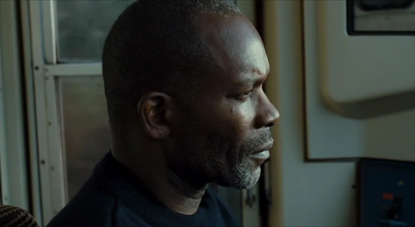 35 Shots of Rum (2008) movie still: closeup — The interior of a train cab with a window visible to the left. A middle-aged man sits in profile while…