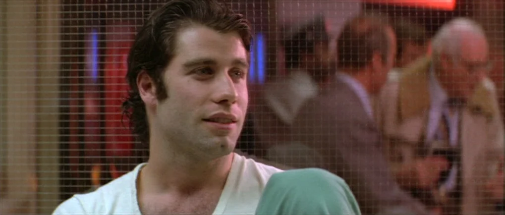 Blow Out (1981) movie still: closeup — A diner booth with a wire-grid partition separating the subjects from the background. A man in a white…