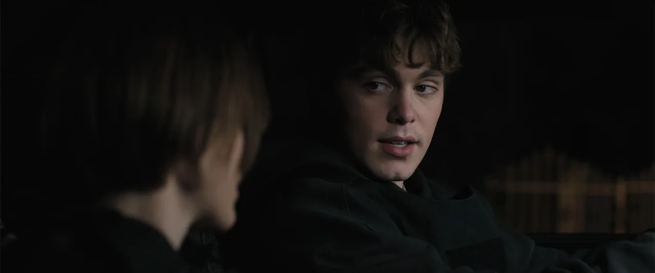 Trap House (2025) movie still: closeup — The interior of a vehicle at night is illuminated by dim, focused light. A young man sits in the passenger…