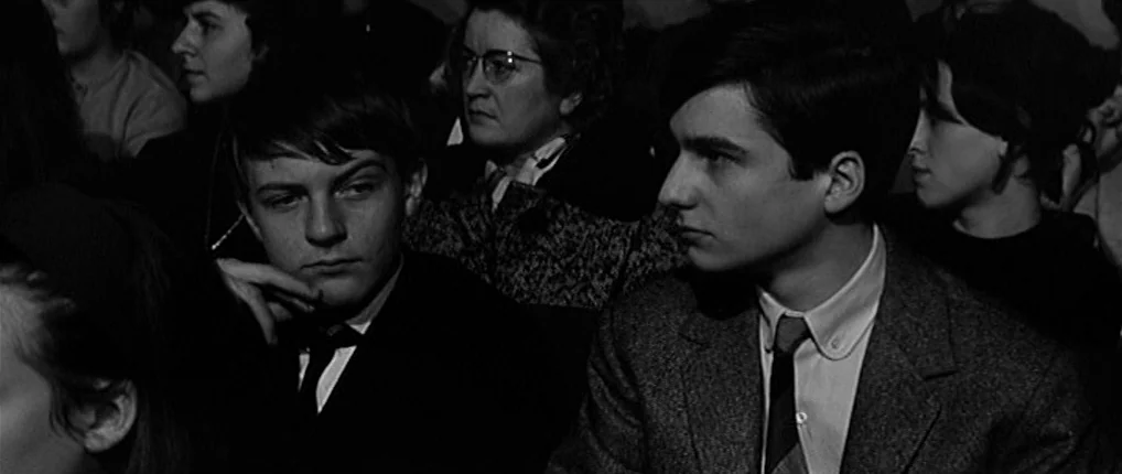 Antoine and Colette (1962) movie still: medium — A crowded auditorium is filled with young people sitting closely together in dark rows. Two boys in…