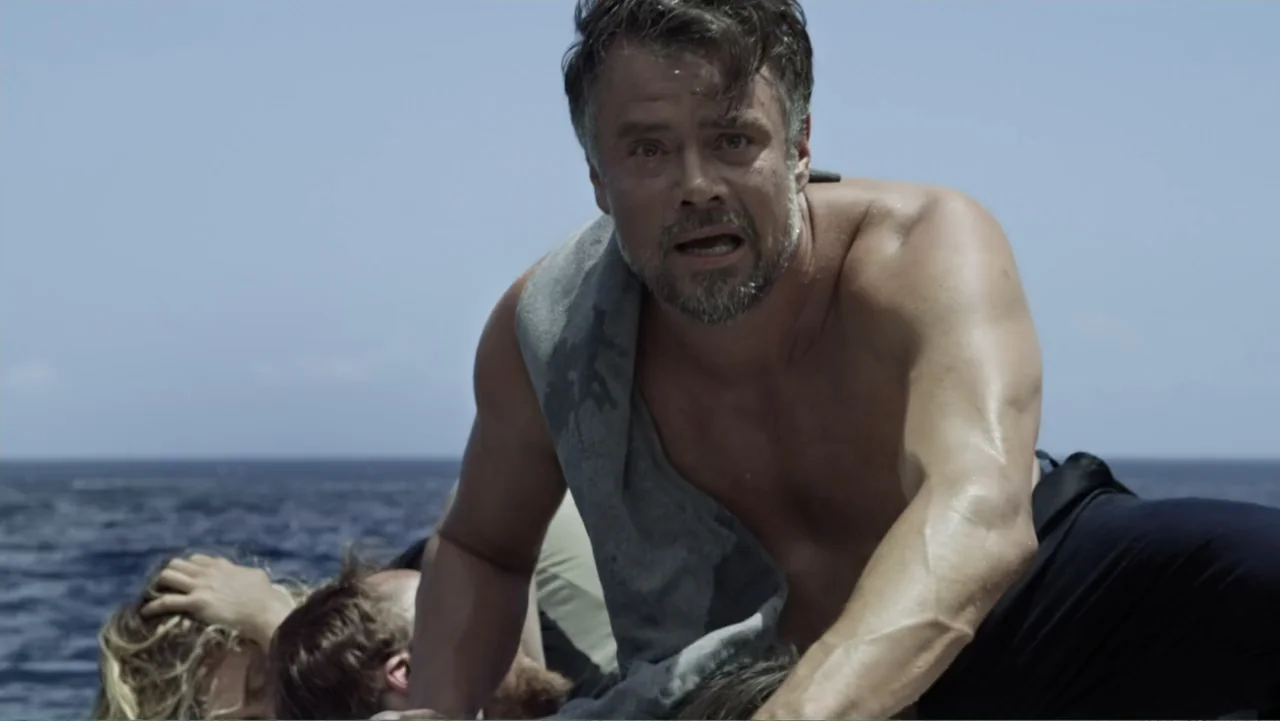 Capsized: Blood in the Water (2019) movie still: medium — A man stands in a boat on open water under bright sunlight. The man looks directly ahead…