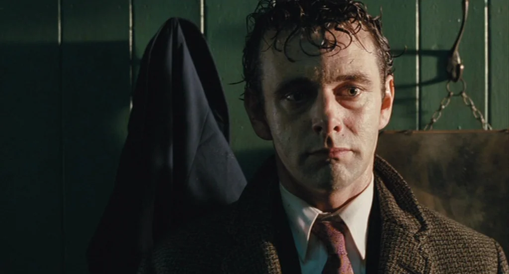 The Damned United (2009) movie still: closeup — A small changing area features vertical dark green wooden wall planks. A man with damp hair wears a…