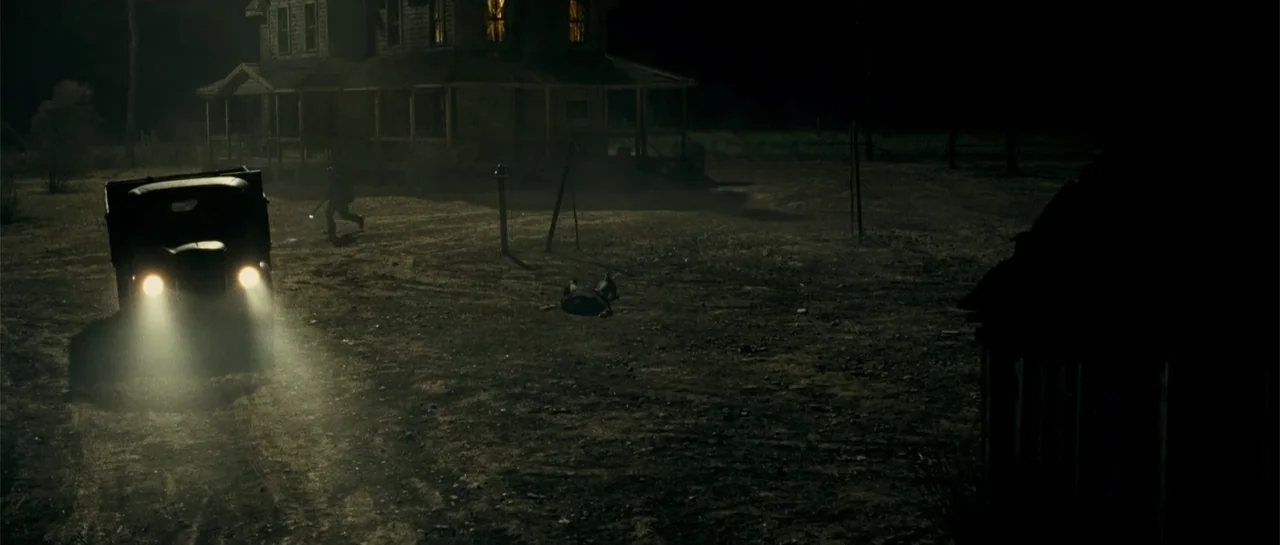 Blood Creek (2009) movie still: wide — A rural landscape features a dark house under moonlight with an idling vintage truck. A person is seen…