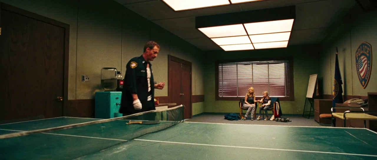 Surveillance (2008) movie still: wide — An institutional room features light green walls, wooden doors, and large square ceiling lights. A police…