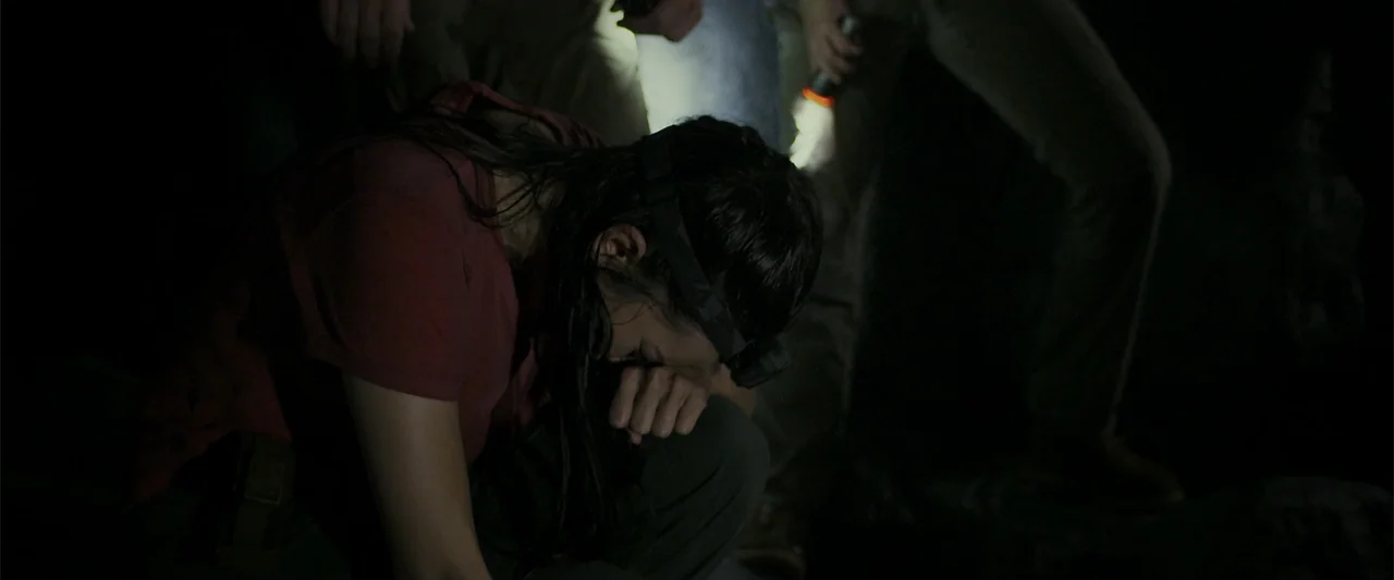Black Water: Abyss (2020) movie still: medium — A dark, rocky subterranean space illuminated by the focused light of headlamps. A young woman…